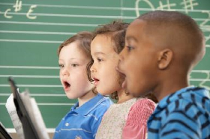 Two schoolboys (5-10) and schoolgirl (5-10) singing in class, close-up